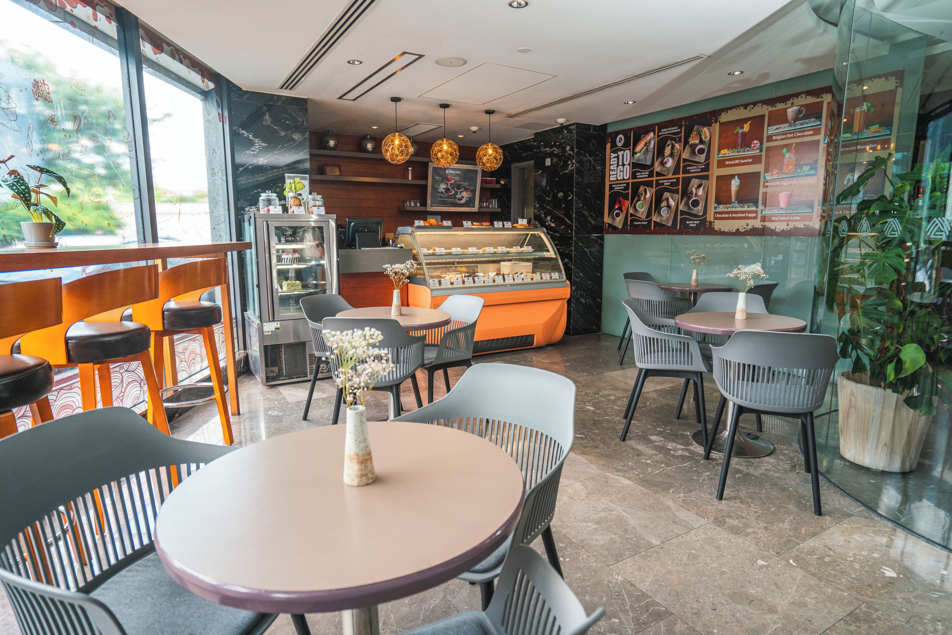 A café interior with round tables, chairs, a display case, and a menu wall.