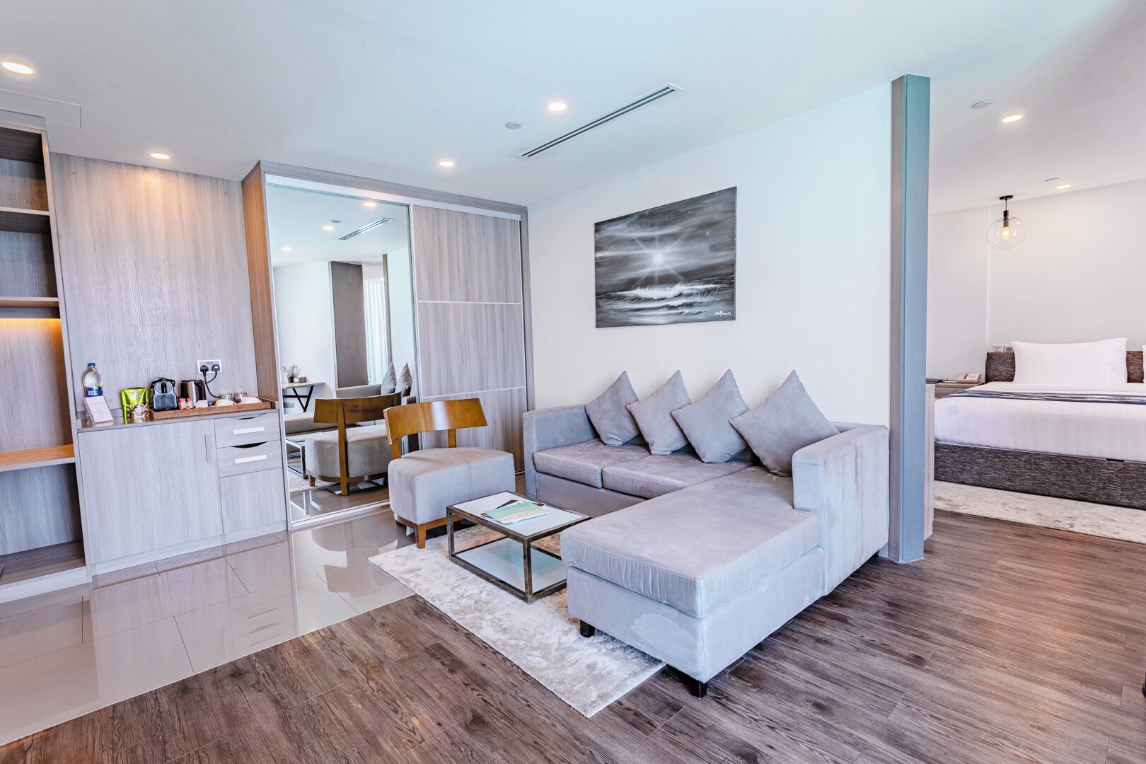 A modern living room with a grey sofa, a coffee table, and a dining area with a wooden table and chairs.