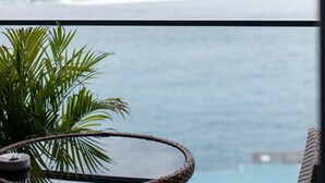 Un balcón con vista al mar, una mesa de mimbre y una planta en maceta.