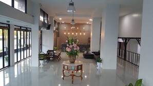 Un lobby espacioso con piso pulido, una mesa central con arreglo floral y una zona de estar con sillas y un sofá.