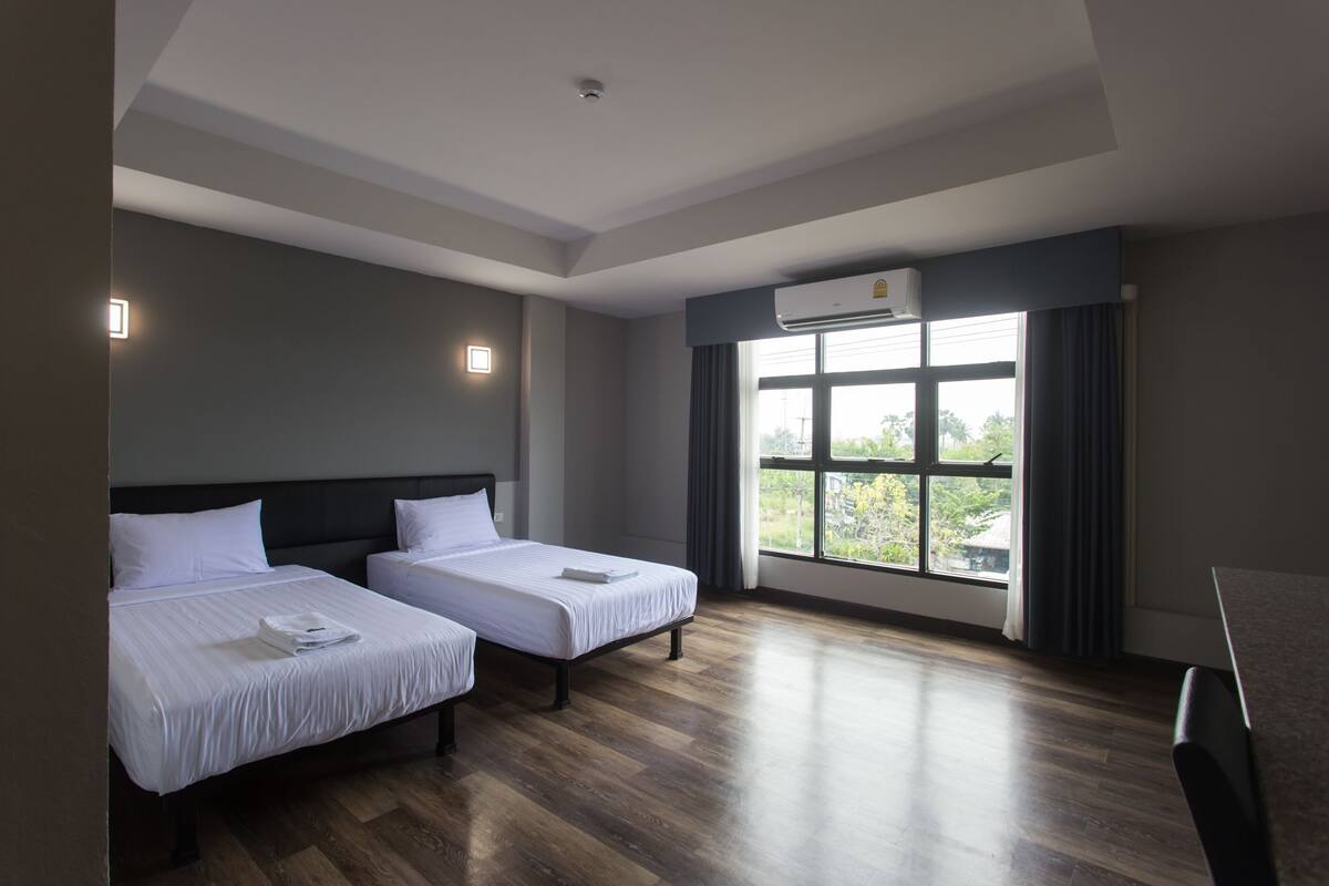 A hotel room with two beds, a large window with a view, and an air conditioning unit.