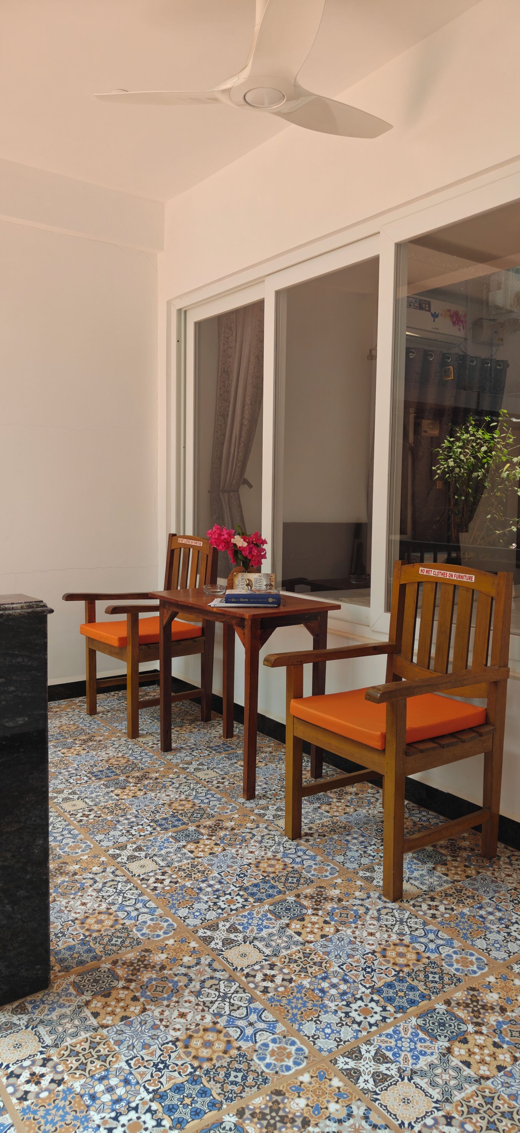 A room with a tiled floor, a table with chairs, a ceiling fan, and a window with curtains.