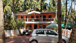 A two-story building with a red and white facade, surrounded by palm trees. - Hilias Retreat (Canacona)