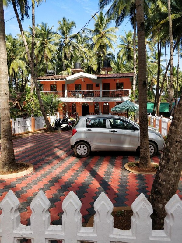 A two-story building with a red and white facade, surrounded by palm trees. - Hilias Retreat (Canacona)