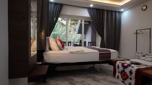 A bedroom with a bed, a bedside table, a mirror, a window with curtains, and a view of palm trees. - Hilias Retreat (Canacona)