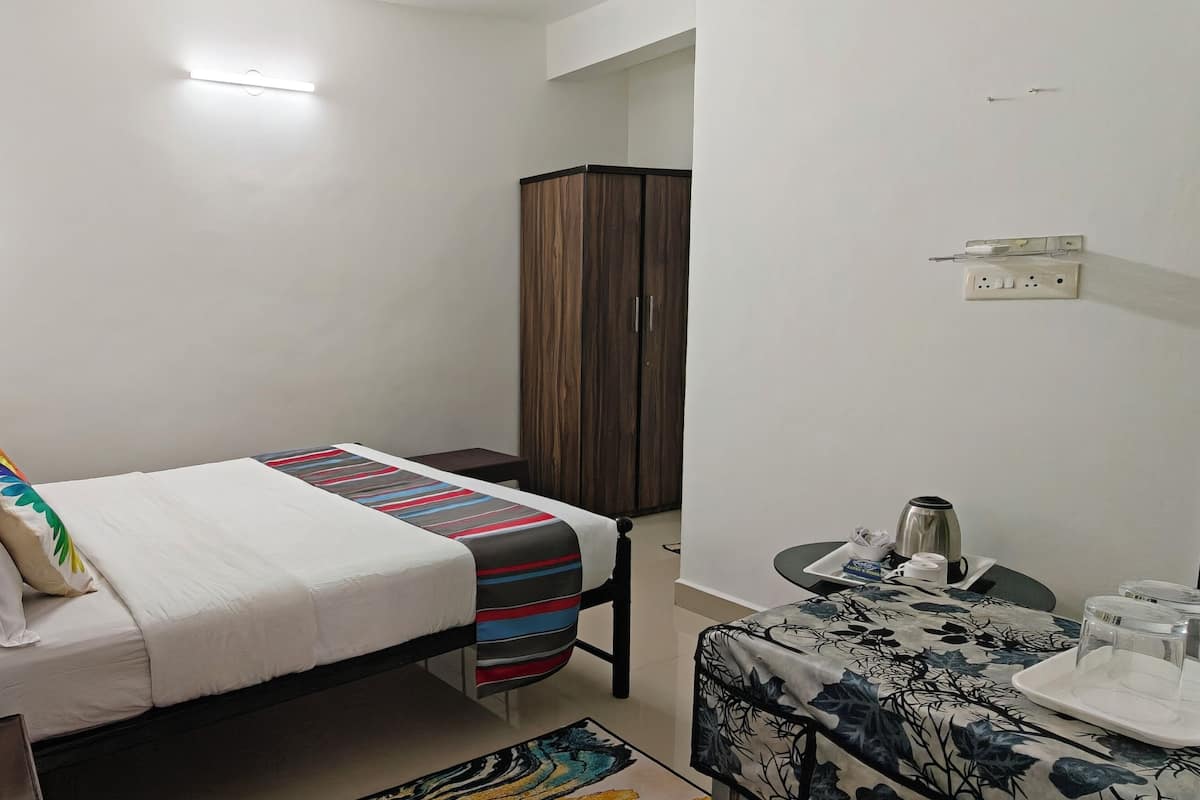 Un lit simple avec une couverture à rayures, une petite table de chevet avec une bouilloire, une armoire et un luminaire fixé au mur.