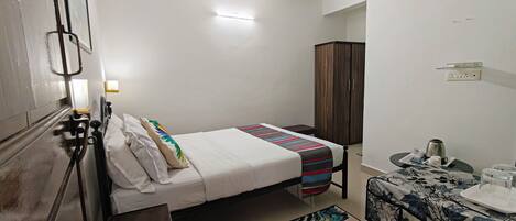 A single bed with a striped blanket, a small bedside table with a kettle, a cabinet, and a wall-mounted light fixture.