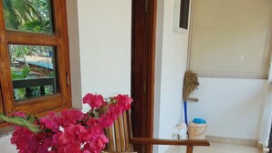 A wooden bench with a vase of pink flowers, a newspaper, and a broom leaning against a wall. - Hilias Retreat (Canacona)