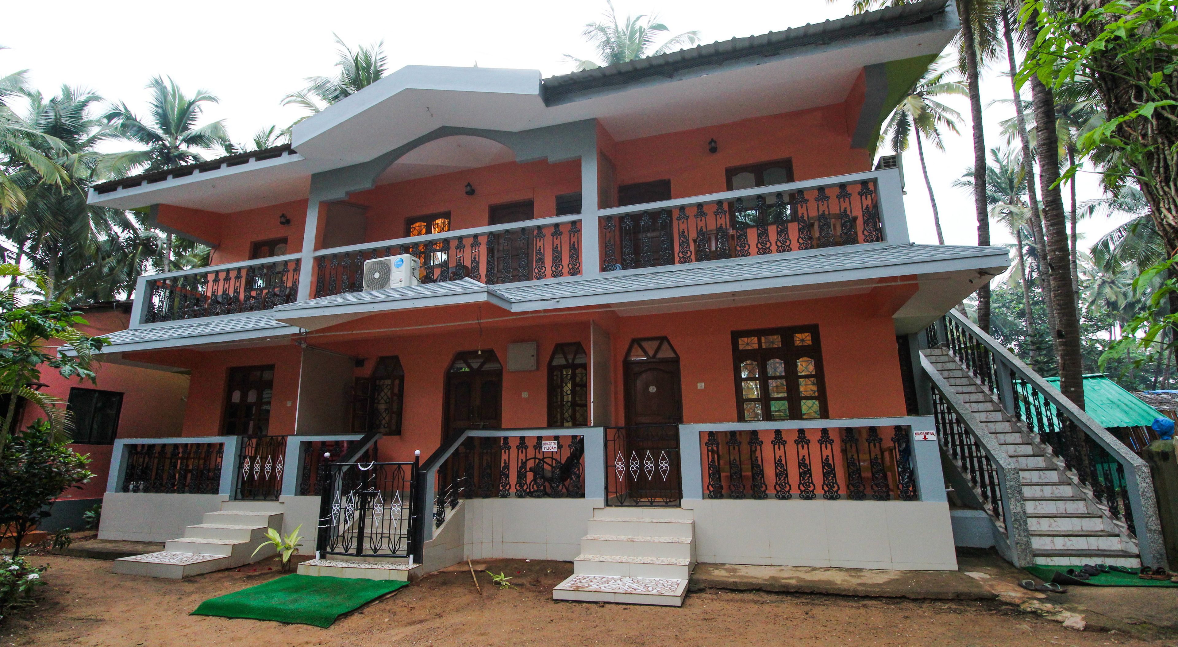 A two-story house with a balcony, a staircase, and a green mat in front.