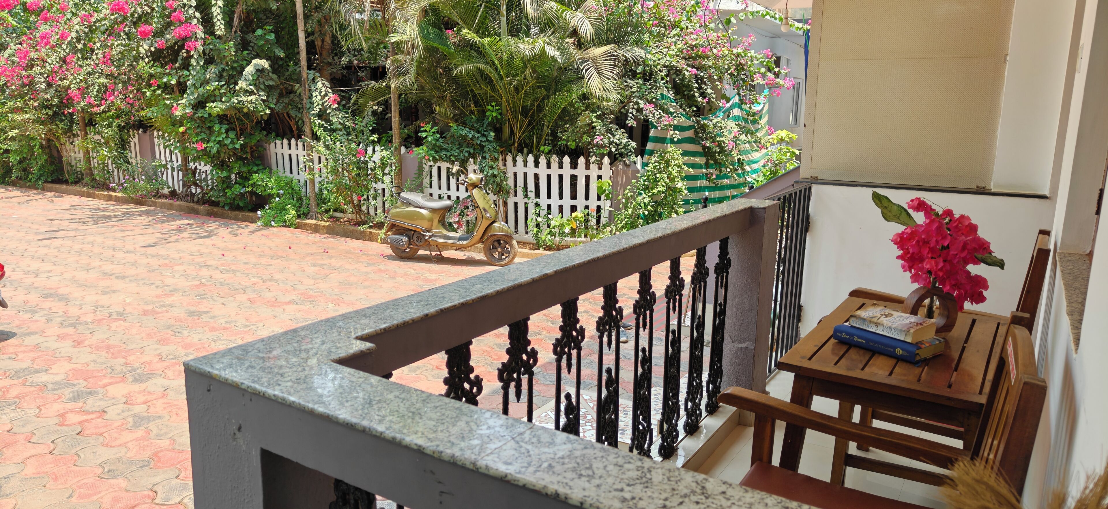 A balcony with a white picket fence, a scooter, and a table with a vase of flowers.
