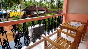 A balcony with a wooden table and chairs, a view of a model village, and a yellow building in the background. - Hilias Retreat (Canacona)