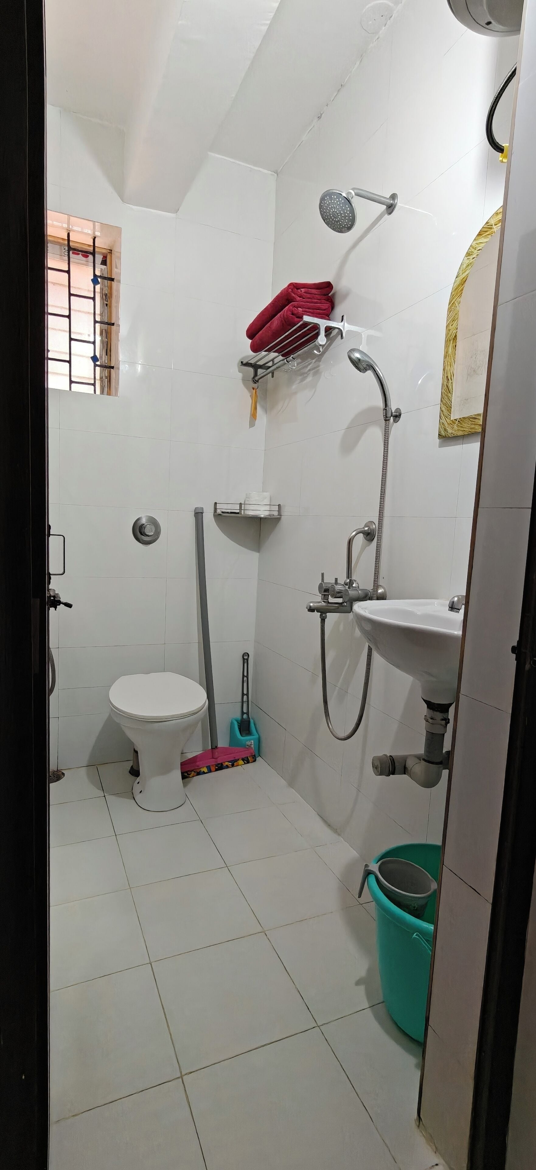Un baño pequeño y limpio con inodoro, lavamanos, ducha y un trapeador.