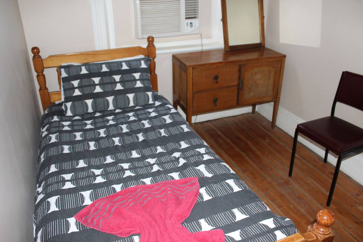 A bedroom with a bed, a dresser, a chair, and a window with blinds.