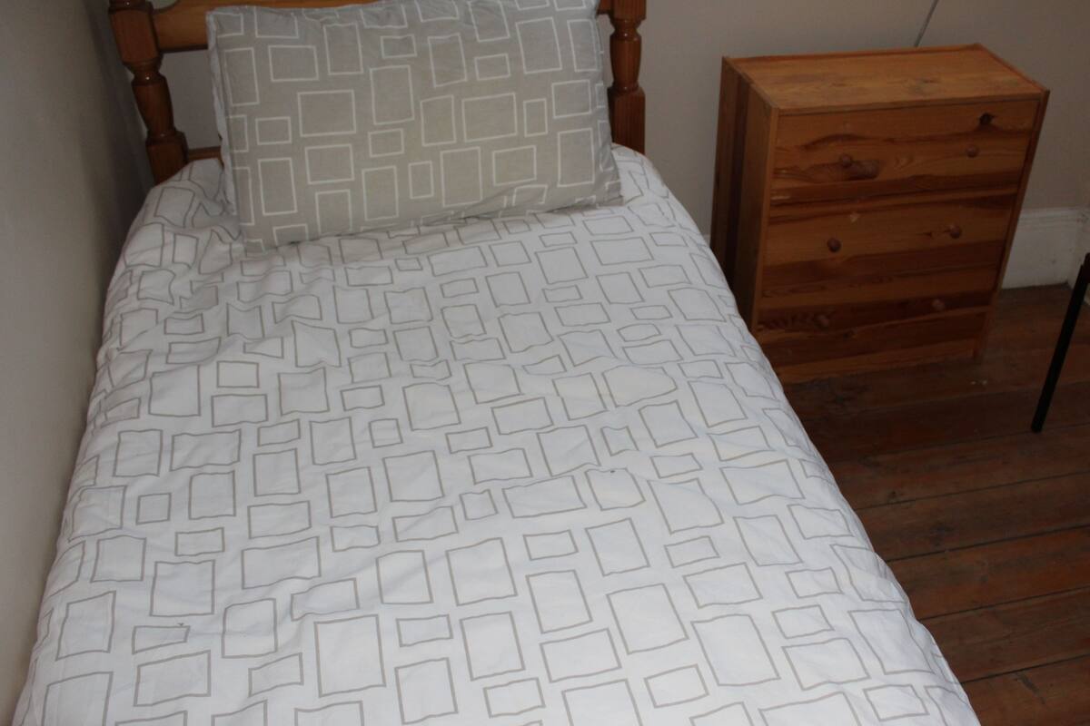 A bed with a patterned bedspread and a wooden nightstand with drawers.