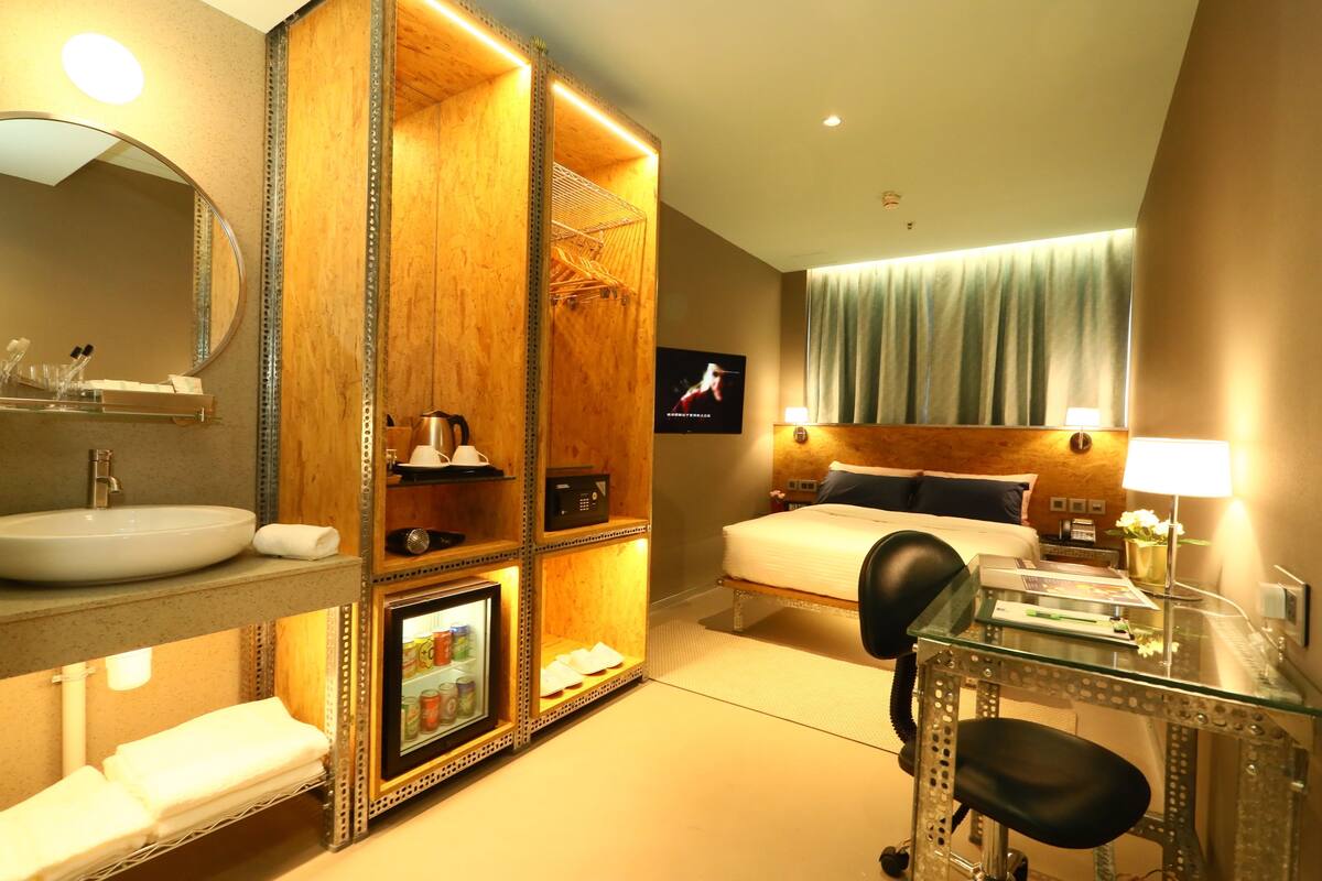 A hotel room with a large bed, a desk with a chair, a vanity with a mirror, a sink, and a television.