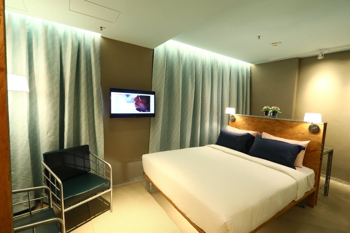 A hotel room with a bed, a television, a chair, and curtains.