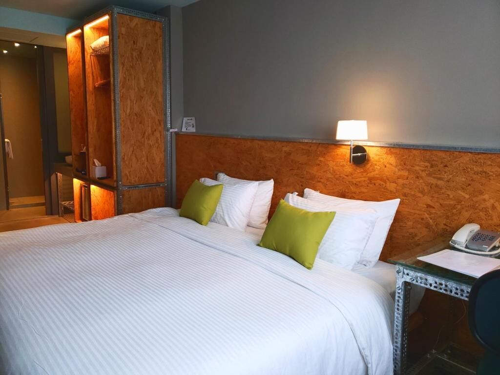 Een hotelkamer met een bed, een nachtkastje met een telefoon en een houten hoofdeinde.