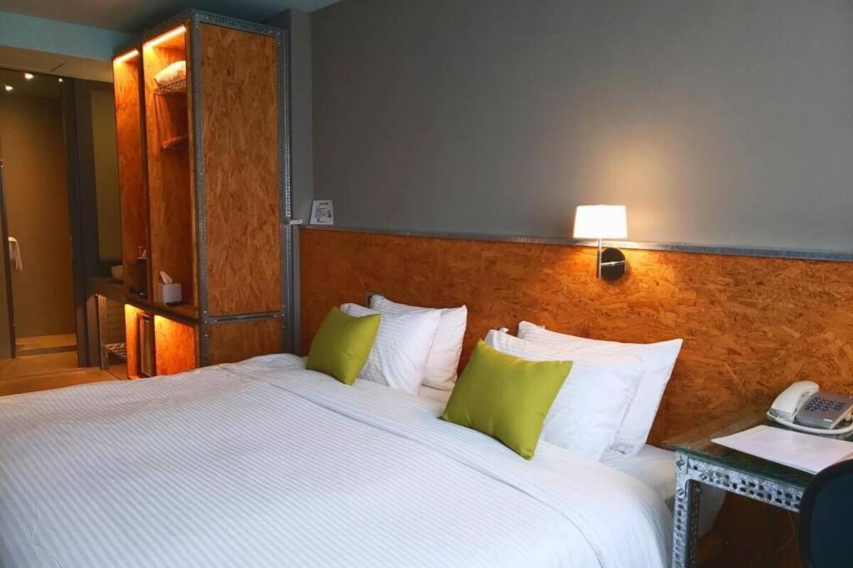 A hotel room with a bed, a nightstand with a phone, and a wooden headboard.