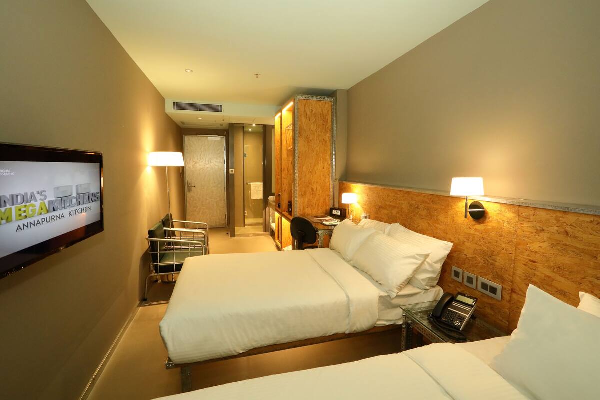 A hotel room with a large bed, bedside tables, a desk, a chair, a TV, and a mirror.