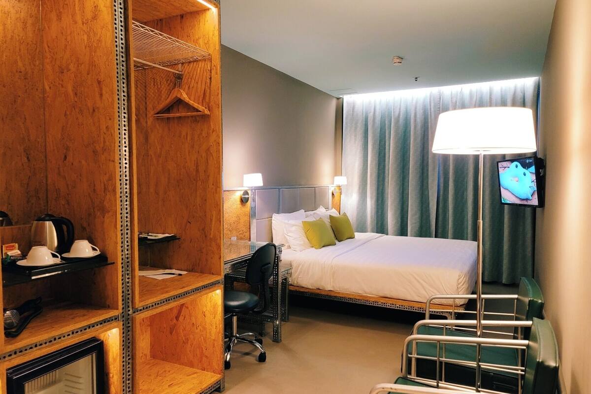 A hotel room with a bed, bedside table, chair, desk, and a TV on the wall.