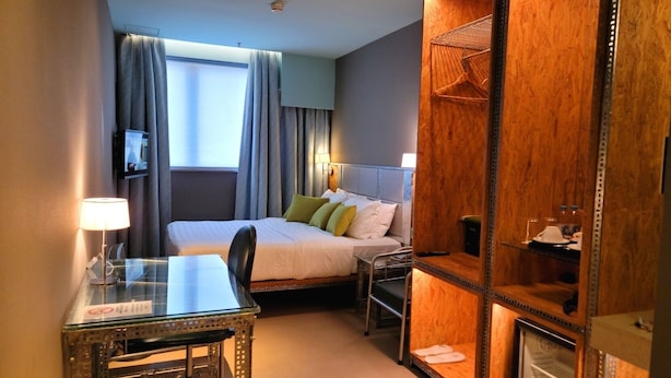 A hotel room with a bed, bedside table, chair, and a built-in TV. - IND Hotel (Kowloon)