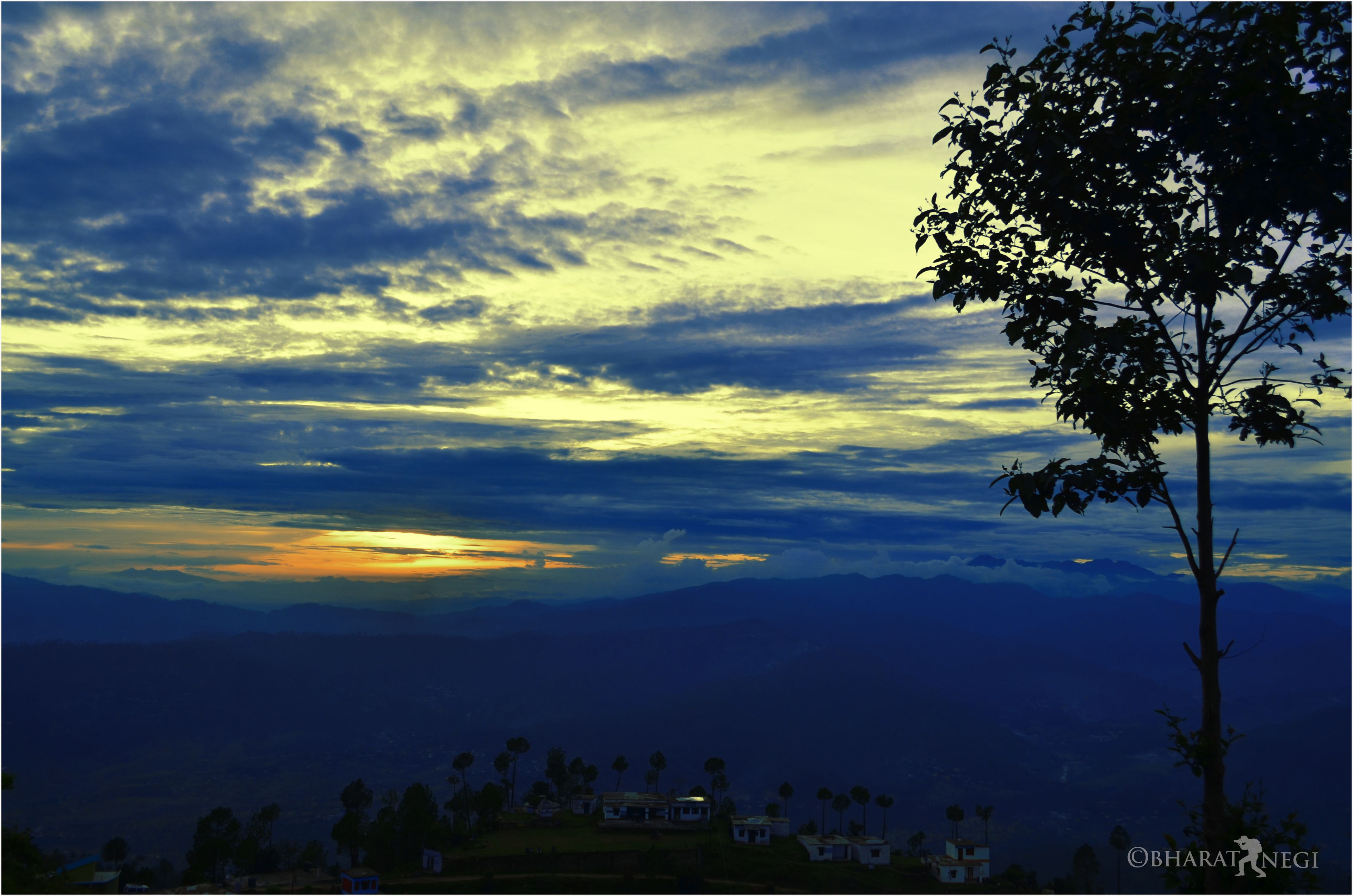 A landscape with a tree and distant buildings, likely a rural or mountainous area.