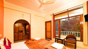 Habitación de hotel con cama, escritorio, silla, ventana con vista a árboles y ventilador de techo.