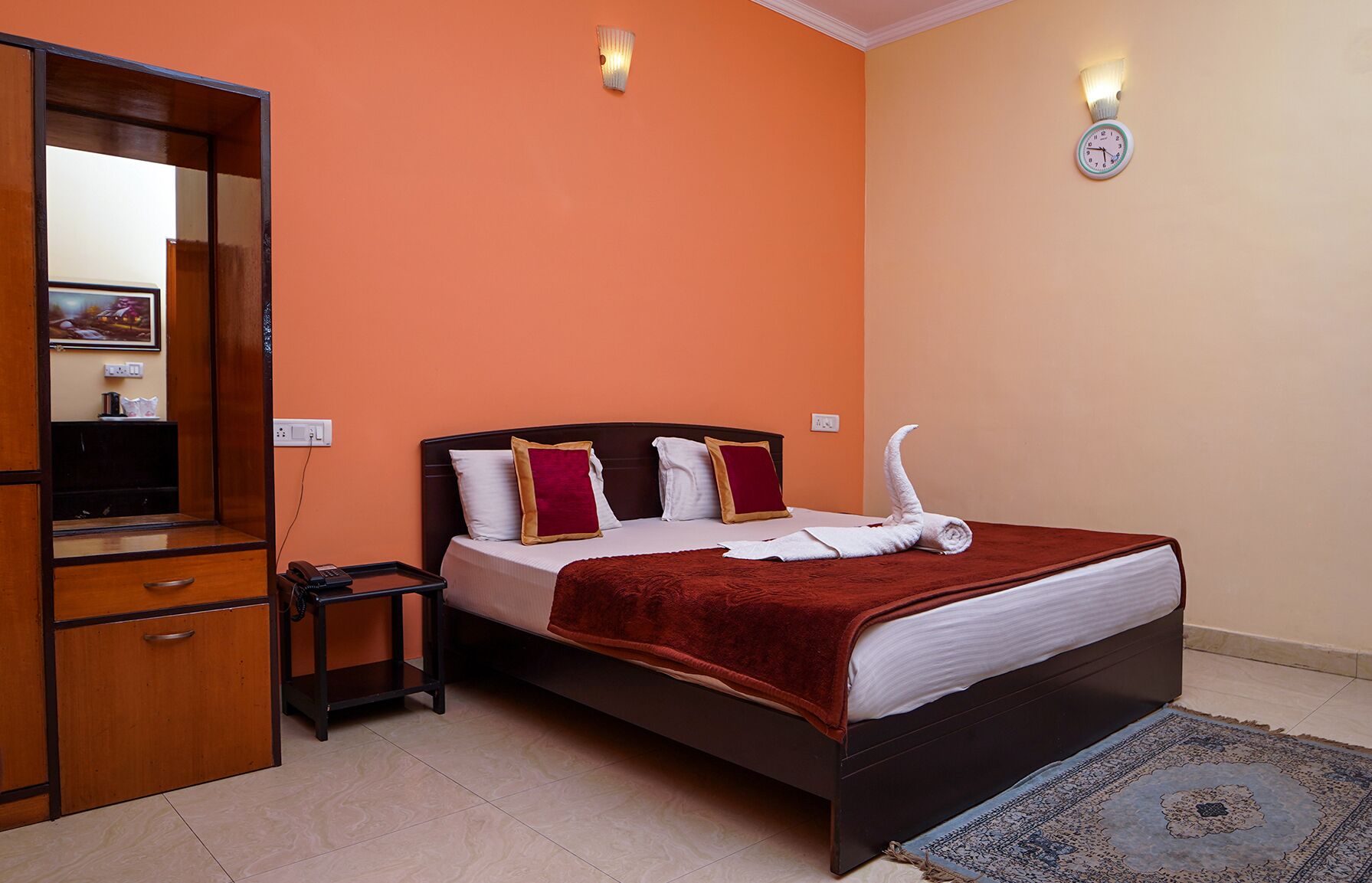 Una habitación de hotel con cama, un armario de madera, una mesita de noche y un reloj de pared.