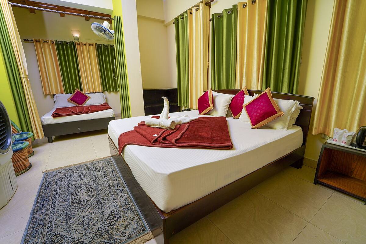 A hotel room with a large bed, a bedside table with a kettle, and a small table with a tray of items.