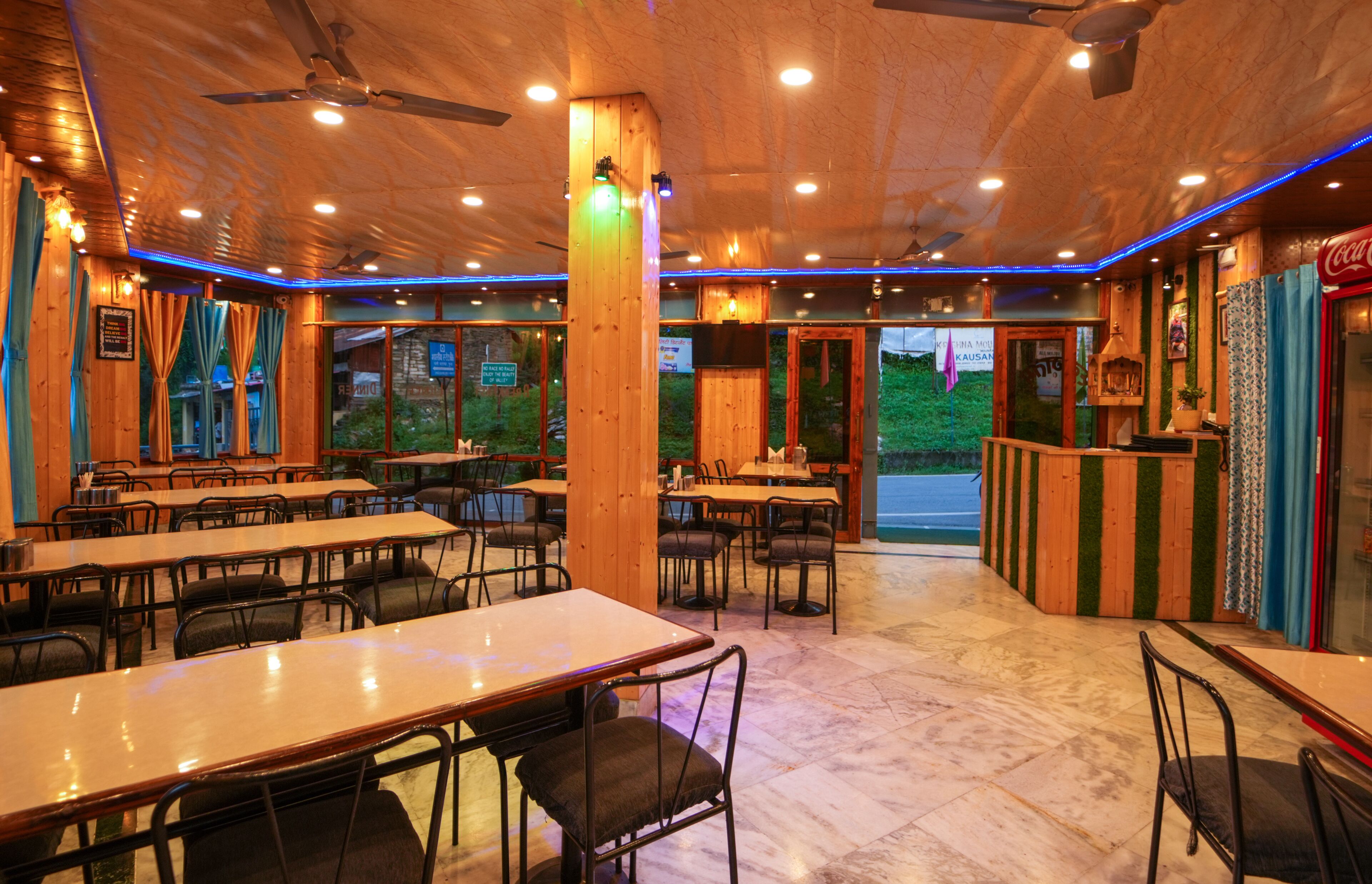Um restaurante com decoração em madeira, várias mesas e cadeiras, e vista para o exterior.