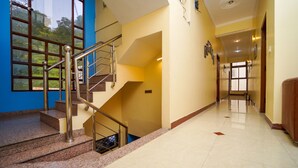 Pasillo de hotel con una escalera, una pared azul y vistas al exterior con vegetación.