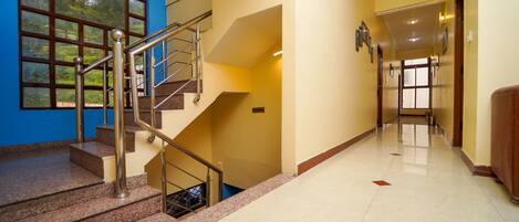 Pasillo de hotel con una escalera, una pared azul y vistas al exterior con vegetación.