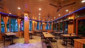 Un restaurante con interiores de madera, varias mesas, sillas y un ventilador de techo.