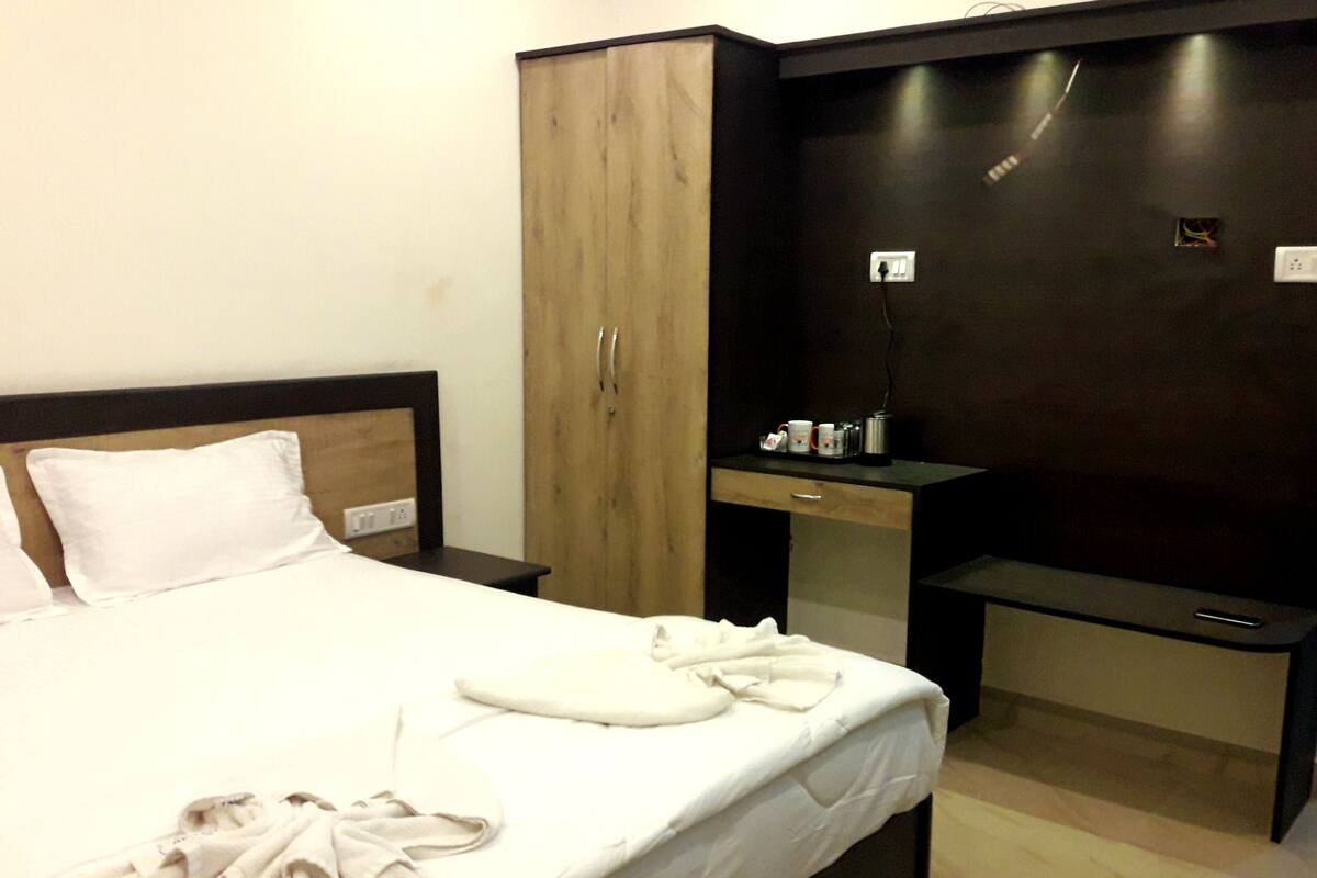 A hotel room with a bed, a wardrobe, a desk with a chair, and a small table with a lamp.