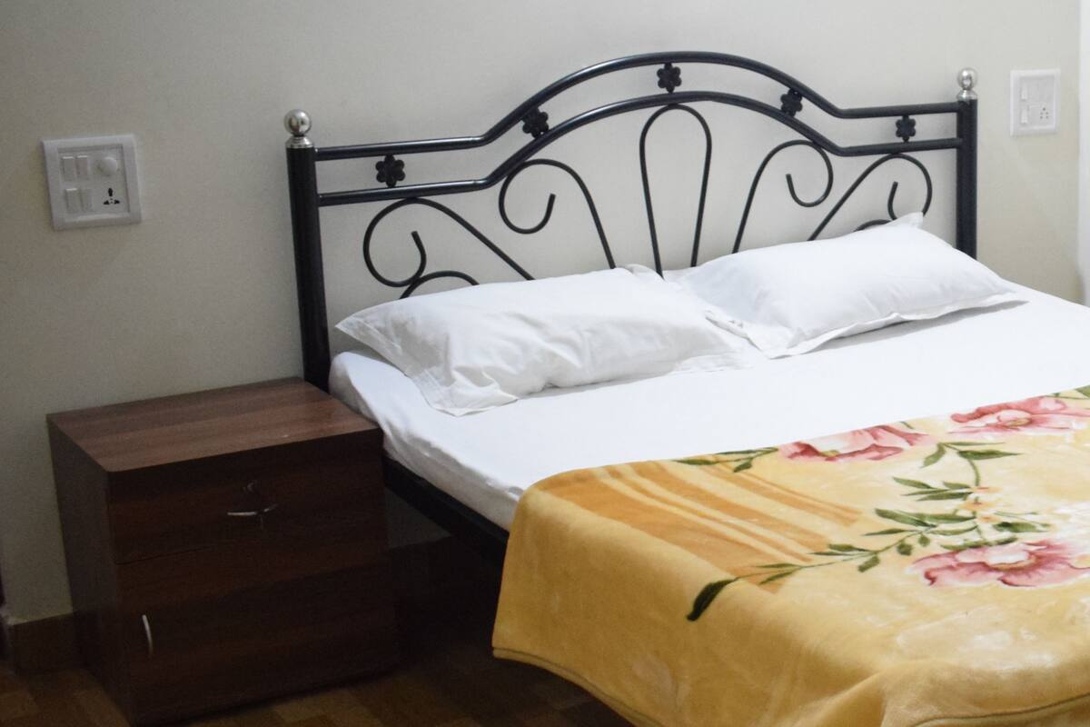 A bed with a floral bedspread, a wooden nightstand with a drawer, and a black metal headboard.