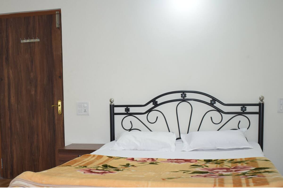 A room with a wooden door, a bed with a floral bedspread, and a black metal headboard.