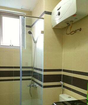 A bathroom with a glass shower enclosure, a toilet, and a wall-mounted heater.