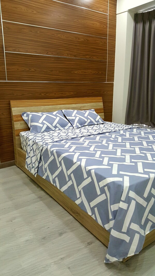 A bed with a geometric patterned bedspread, wooden headboard, and a grey curtain.