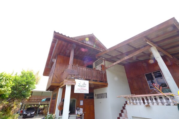 Edificio de dos pisos con un balcón, un letrero que indica 'Home Stay' y una escalera que lleva al piso superior.