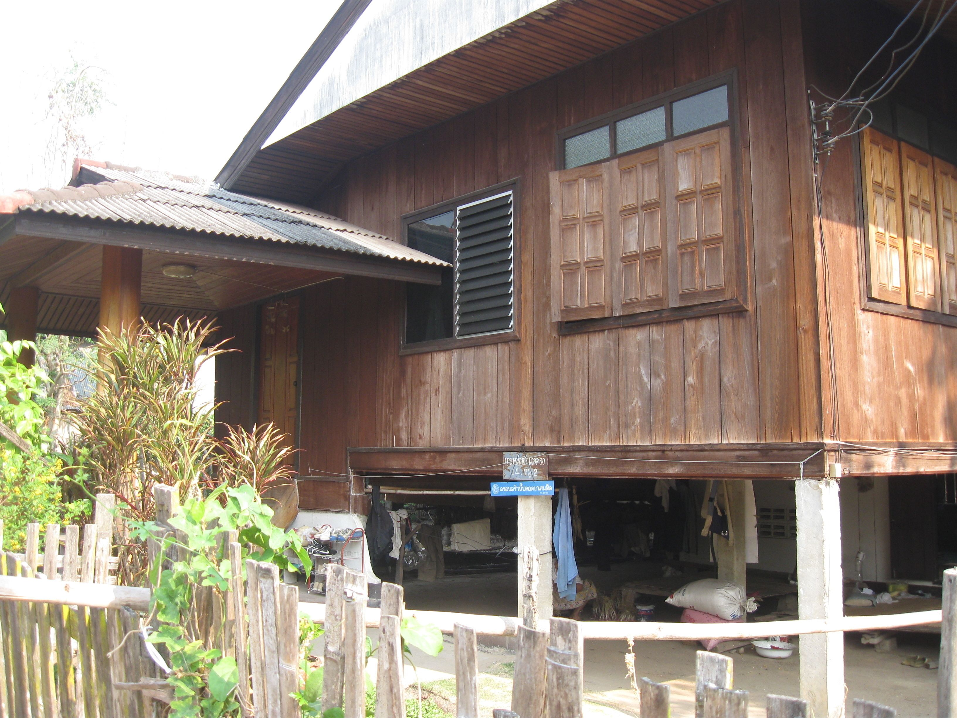 A wooden house with a porch, a window with shutters, and a signboard.