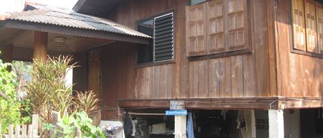 A wooden house with a porch, a window with shutters, and a signboard.