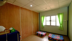 Una habitación con piso de madera, un armario azul, un ventilador y dos colchones coloridos.