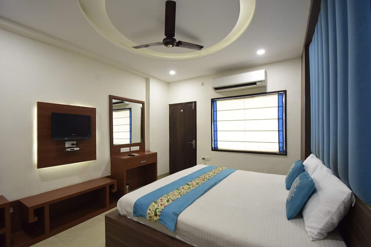 A modern hotel room with a bed, a TV mounted on the wall, a ceiling fan, and an air conditioning unit.