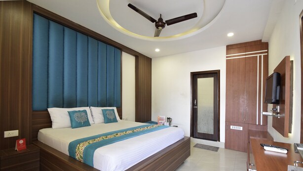 Habitación de hotel con una cama grande, cabecero de madera, ventilador de techo, televisor y escritorio con un cartel que indica el número de habitación 202.