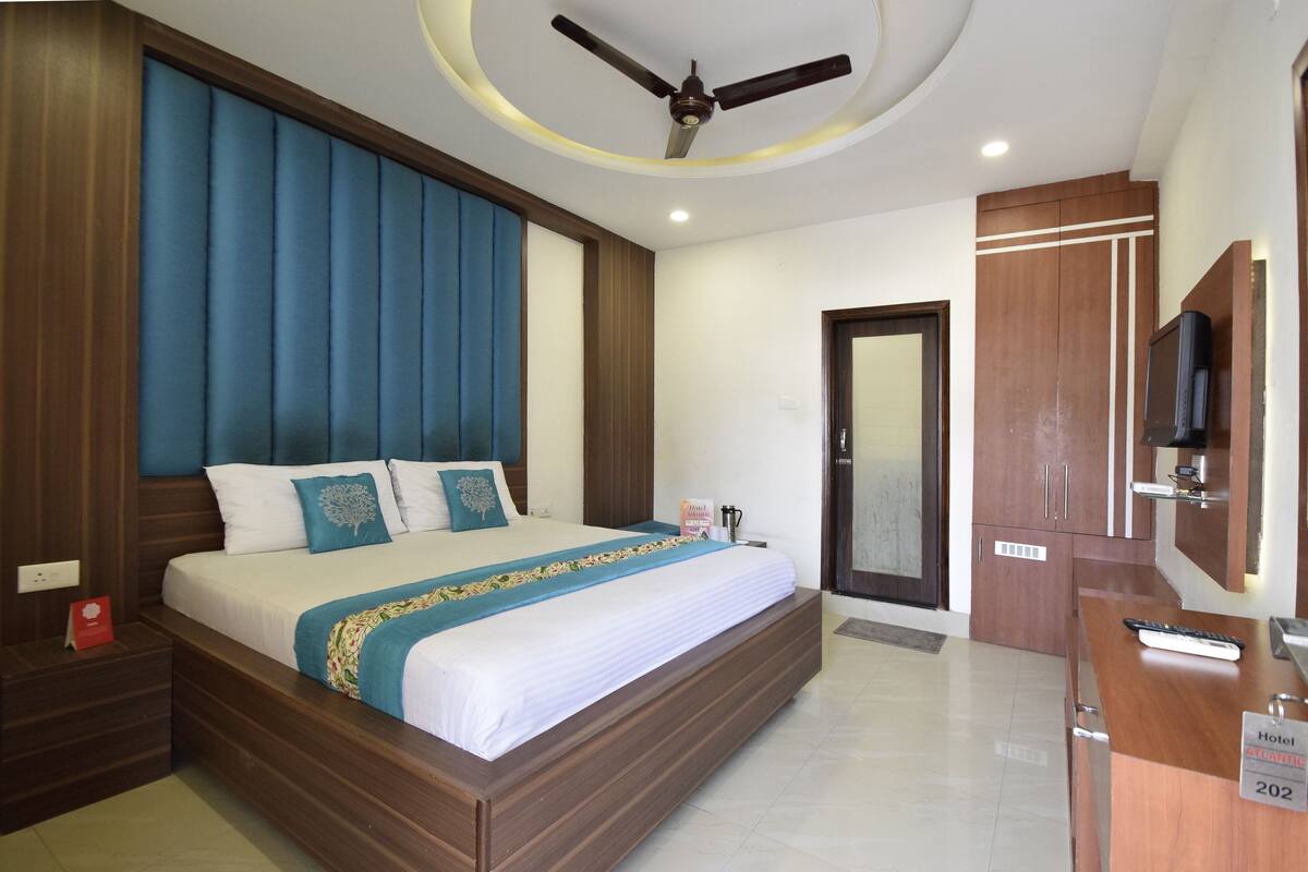 A hotel room with a large bed, wooden headboard, a ceiling fan, a TV, and a desk with a sign indicating room number 202.