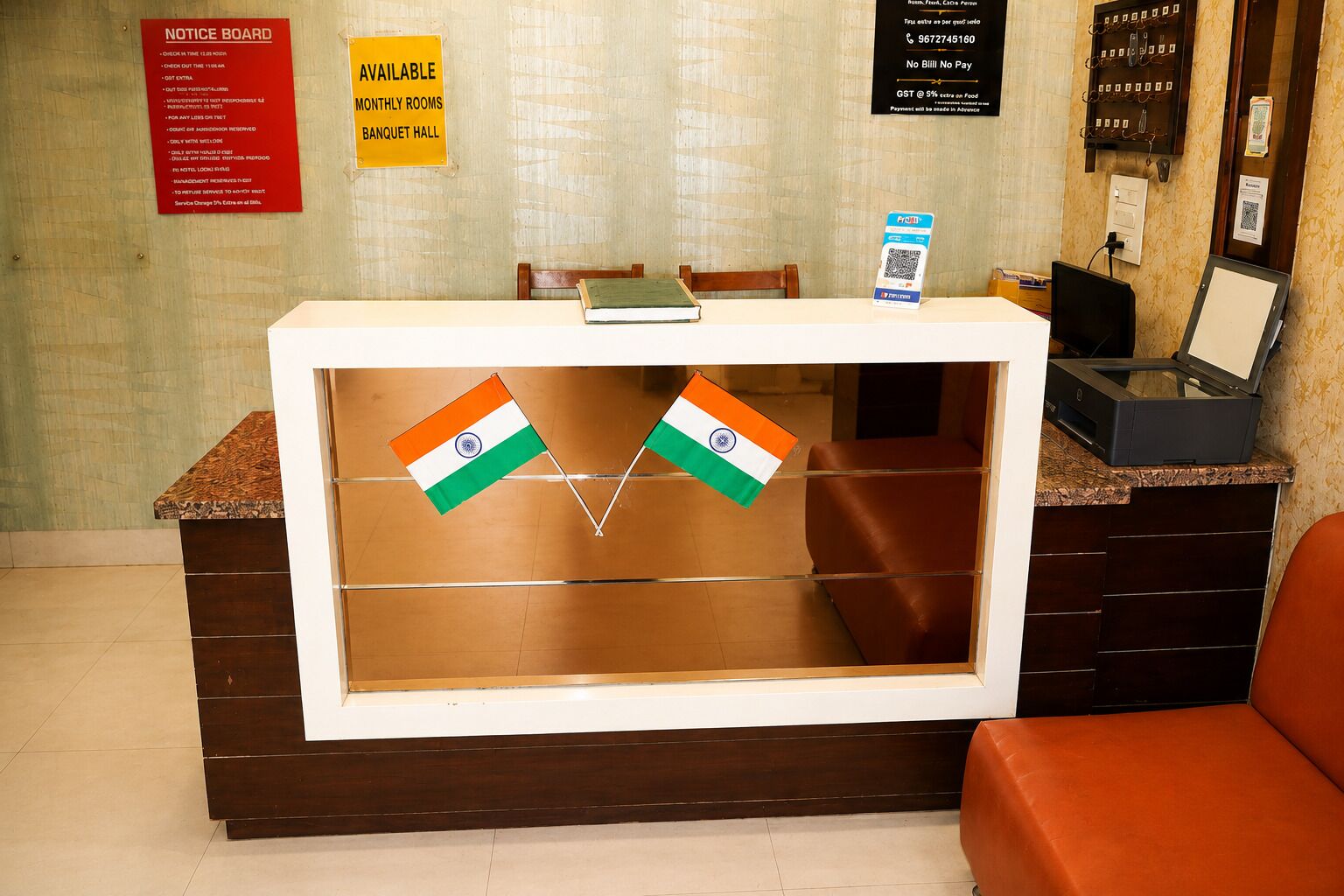 Una recepción con un tablón de anuncios, un letrero que indica habitaciones mensuales disponibles y salón de banquetes, y dos banderas indias.