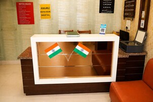 Una recepción con un tablón de anuncios, un letrero que indica habitaciones mensuales disponibles y salón de banquetes, y dos banderas indias.