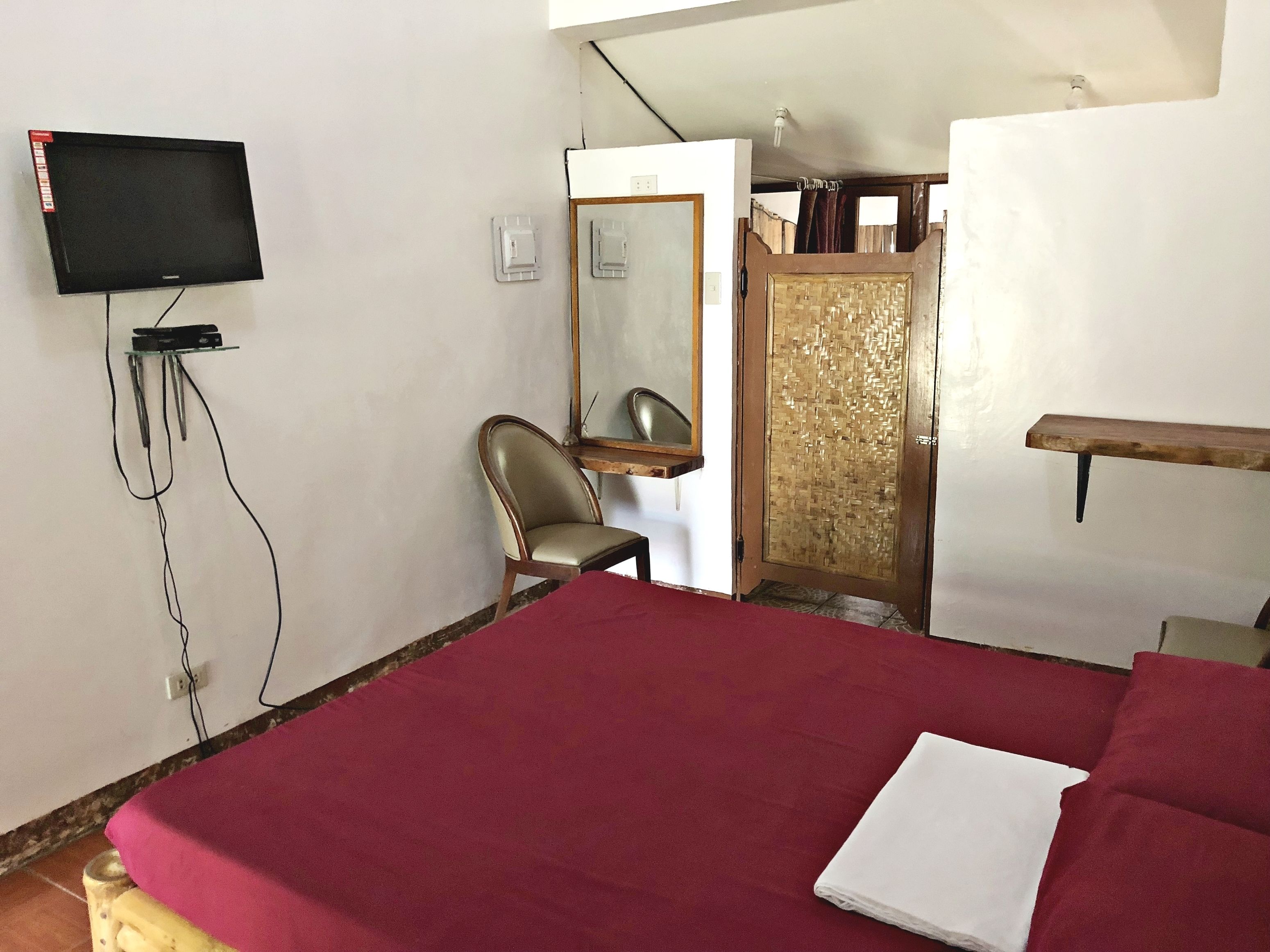 A bedroom with a bed, a chair, a television mounted on the wall, and a wardrobe.