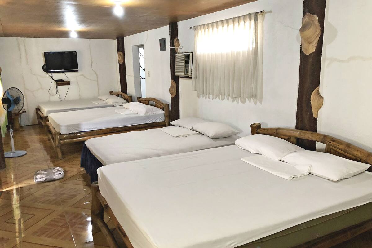 A hotel room with three wooden beds, a television mounted on the wall, and a ceiling fan.