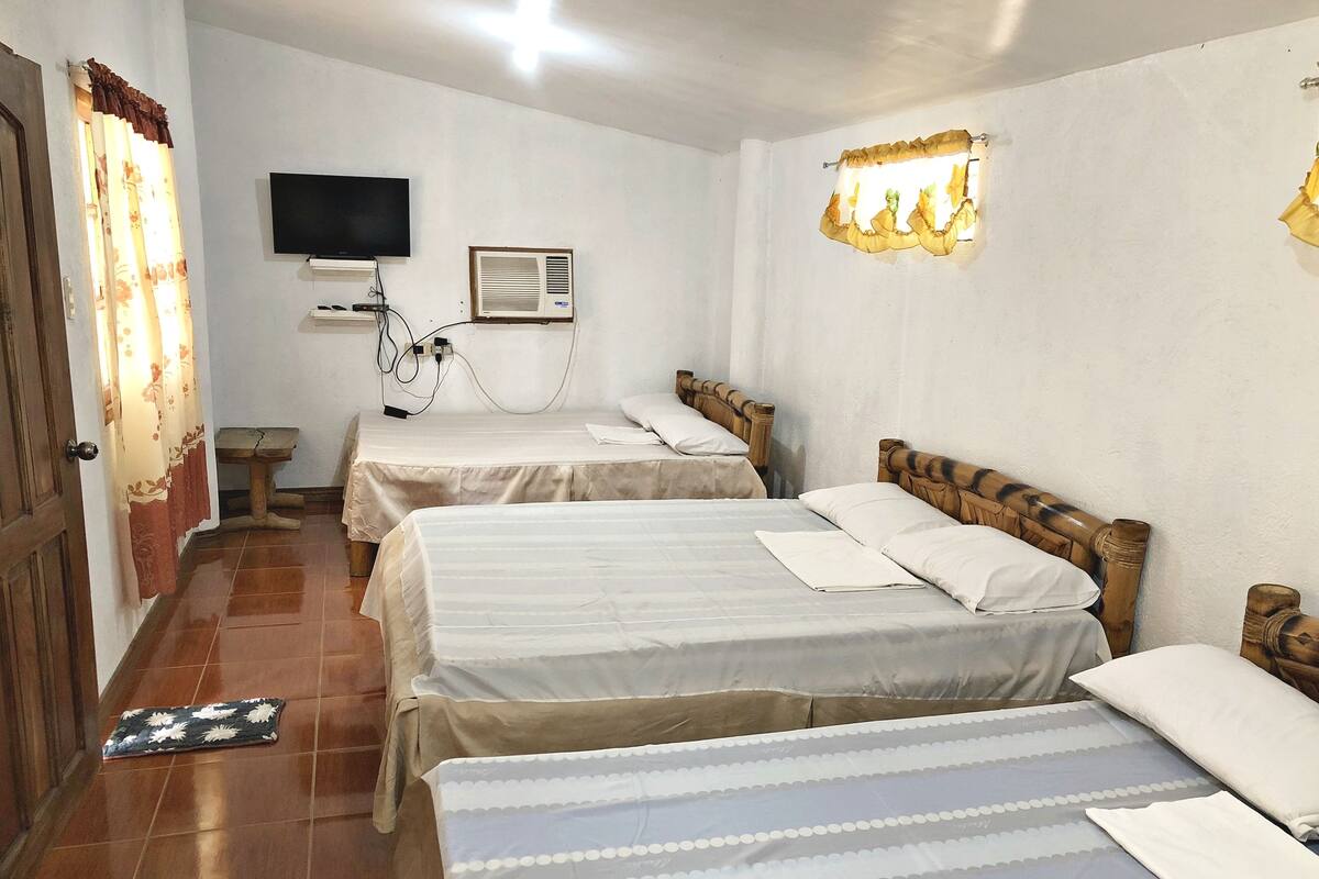 A hotel room with two beds, a TV, an air conditioning unit, and a bedside table.